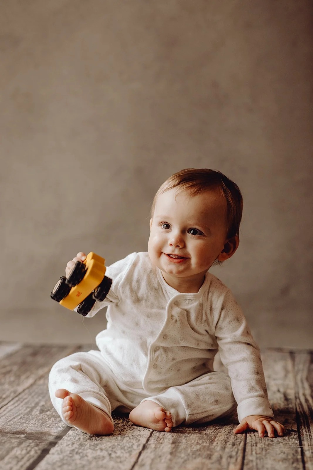 Lachende baby die rechtop zit op een houten vloer met een gele tamboerijn